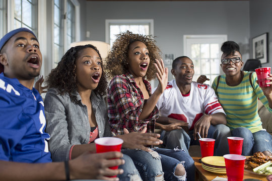 Five adult friends gasping whilst watching TV from sofa