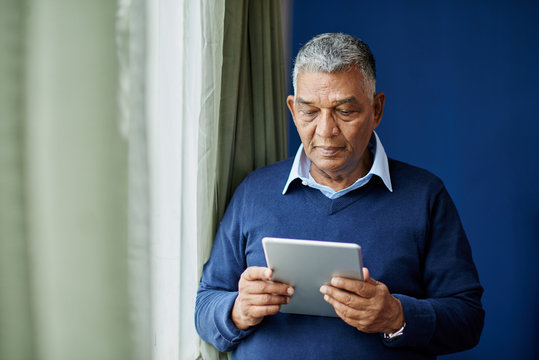 Pensive Old Man With Digital Tablet Standing At Window