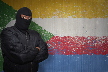 dangerous man in a mask standing near a wall with painted national flag of comoros
