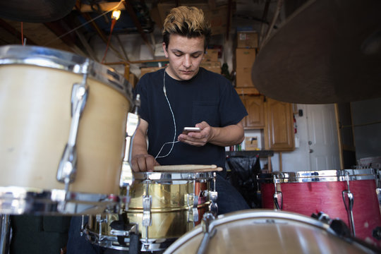Young male drummer in basement reading smartphone texts