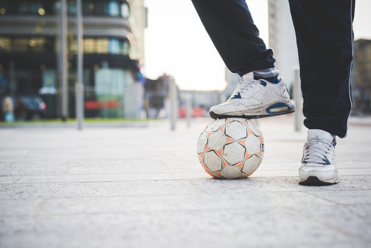 Low section of man standing with soccer ball at his feet on city street