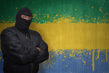 dangerous man in a mask standing near a wall with painted national flag of gabon