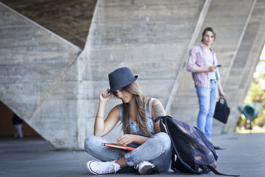 Female student sitting on floor with book, man watching