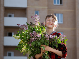 Happy girl with big bouquet of flowers laughing happily in the sun on a background of a new, multi-storey building - new building. Concept - happiness, joy, buying apartments, new housing