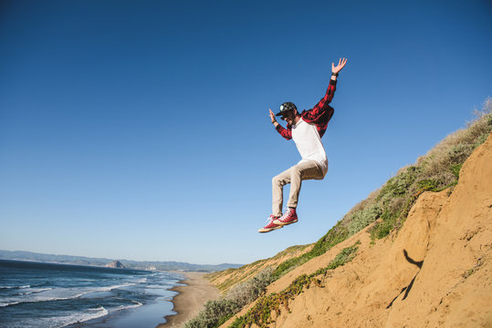 Young man jumping down sandy hill, in mid air