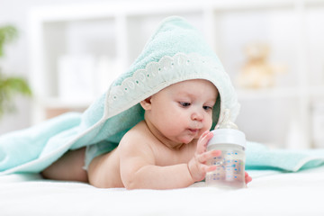 Baby drinks water from bottle covered towel after bath