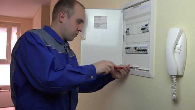 Man with screwdriver turn on cutout and close panel door.