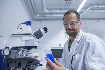 Lab assistant looking at tube of blue liquid
