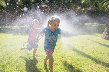Boy running after girl in garden with water sprinkler
