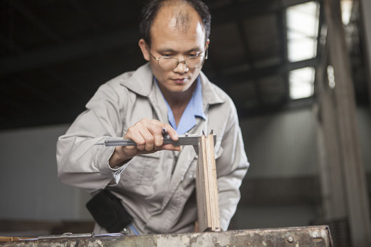 Carpenter measuring wood plank with vernier caliper in factory, Jiangsu, China