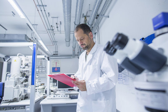 Lab assistant checking details on clipboard