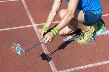 Athlete crouching at the starting line of a running track taking selfie with his mobile phone on a selfie stick