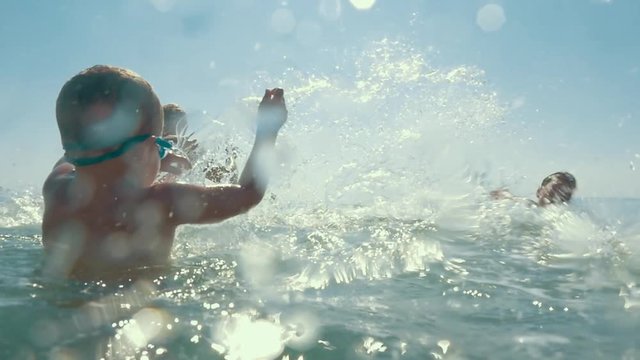 Slow motion shot of united parents and child playing in the sea splashing water.