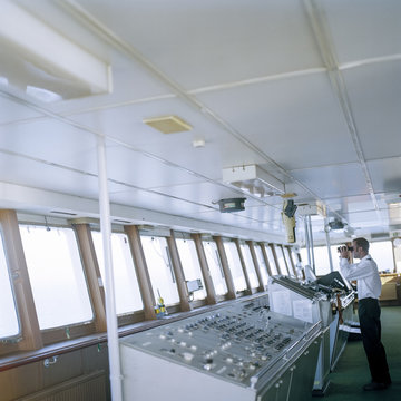 Sailor using binoculars on bridge of container ship at sea