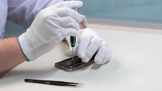 Repairman in white gloves disassemble smartphone with screwdriver