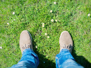 Summer is coming! Male boots on the grass with first flowers. Top view.