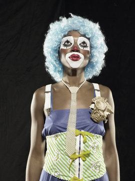 Studio portrait of young woman wearing clown face paint and blue wig looking up