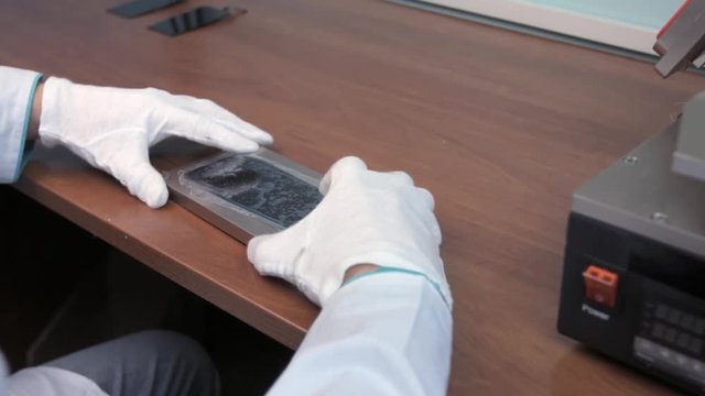 Repairman remove protection film from smartphone LCD display and put it under the mechanical press