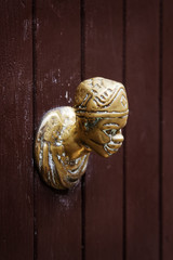 Antique door knocker in the shape of a human head on a wooden door in Venice, Italy