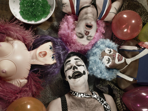 Overhead view of three adults wearing clown face paint and wigs with blow up doll