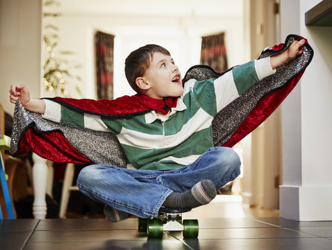 Young boy sitting on skateboard wearing cape