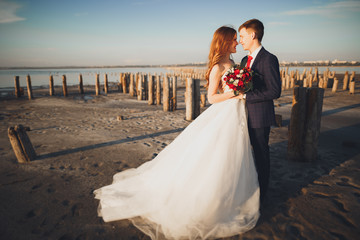 Beautiful young wedding couple, bride and groom posing near wooden poles on the background sea