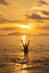 Woman standing on the sea in sunset with hand raised up