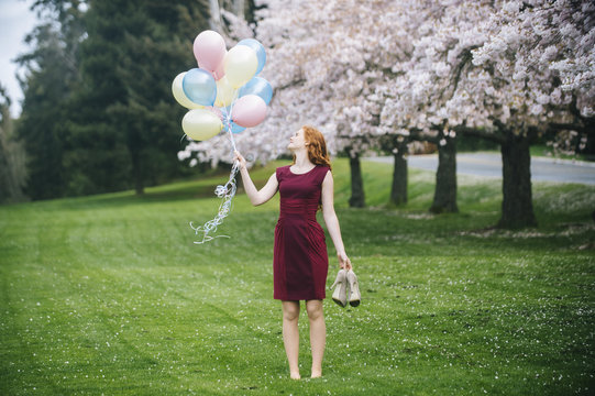 Young woman holding bunch of balloons in spring park