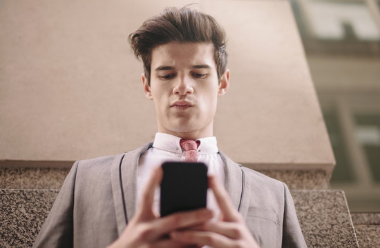 Low angle view of young city businessman reading smartphone text