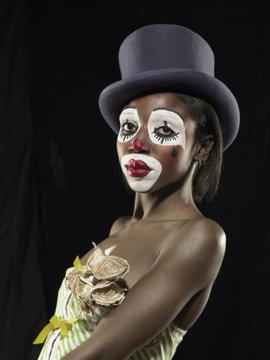 Studio portrait of young woman in clown face paint wearing top hat