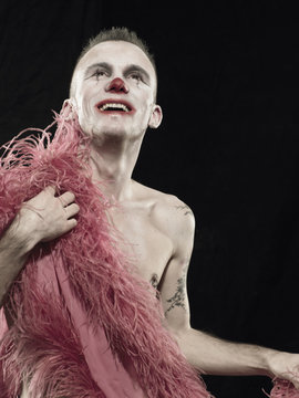 Studio portrait of young man in clown face paint with pink feather boa