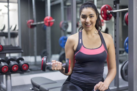 Portrait of a smiling young woman at gym holding dumbbell