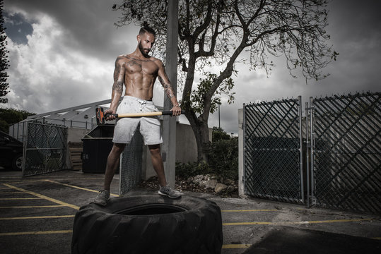 Poised male boxer standing on truck tyre holding sledge hammer in yard