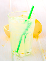 glass of lemonade with straw on wood