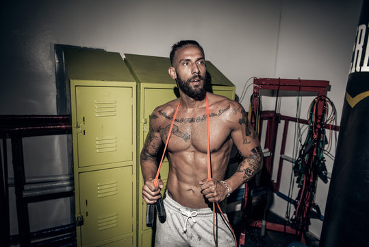 Tattooed male boxer with skipping rope in gym - Powered by Adobe