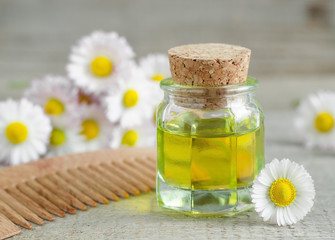 Small bottle of cosmetic chamomile oil and wooden hair comb