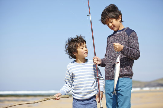 Two young boys standing together, holding fishing rod and fish