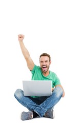 Happy young man raising his fist while using laptop