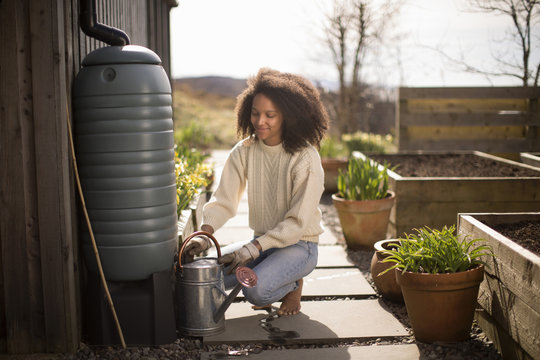 Mid adult woman filling watering can from water butt