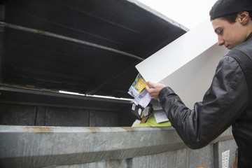 Teenage boy emptying bin with paper waste to recycling bin