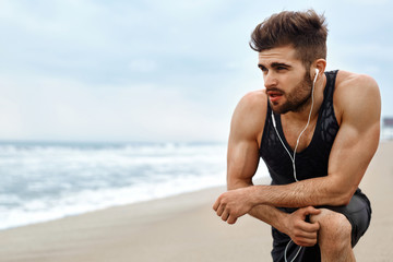 Portrait Of Athletic Man With Fit Muscular Body Resting After Jogging On Beach. Tired Exhausted Male Runner Taking A Break, Breathing After Running Workout Outdoor Near Ocean. Sports, Fitness Concept