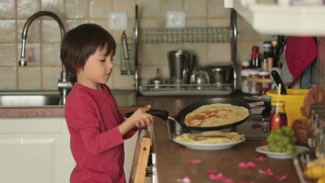 Sweet preschool child, helping his mom in the kitchen, making pancakes in the morning, happy childhood