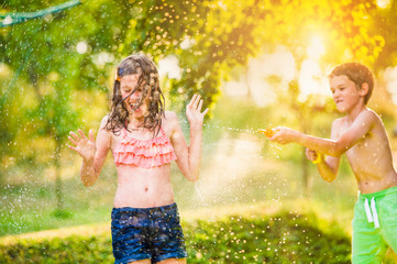 Boy splashing girl with water gun, sunny summer garden