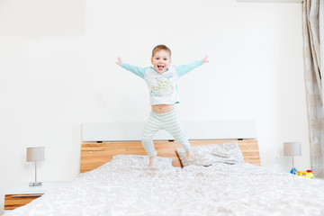 Cheerful little boy showing tongue and jumping on bed