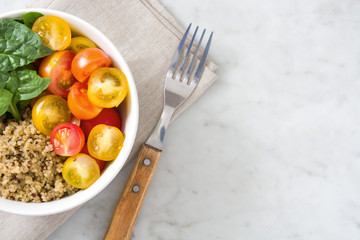 Quinoa salad in bowl, tomatoes and spinach on marble table

