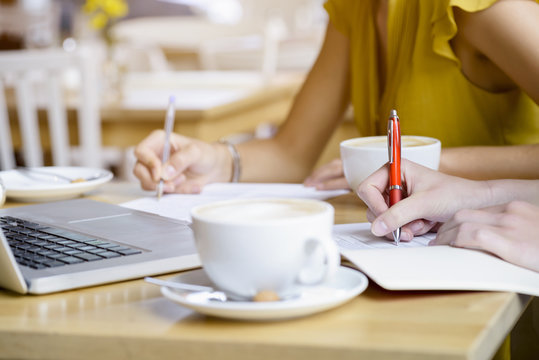 Cropped close up of two young women in cafe writing notes