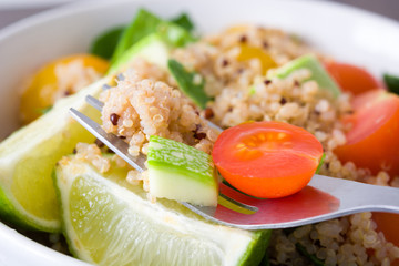 Quinoa salad in bowl, tomatoes and spinach on white wooden table
