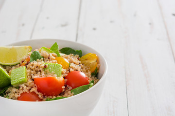 Quinoa salad in bowl, tomatoes and spinach on white wooden table
