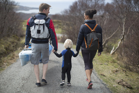 Family walking on country road holding hands, rear view