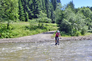 Dziewczyna na rowerze przejeżdża przez rwący potok © Jurek Adamski